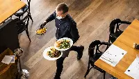 Cameriere di un ristorante serve i clienti protetto dalla mascherina facciale